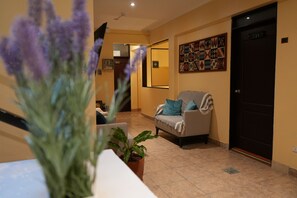 A reception area with a sofa, a potted plant, and a door with room numbers. - Posada Miraflores (Lima)