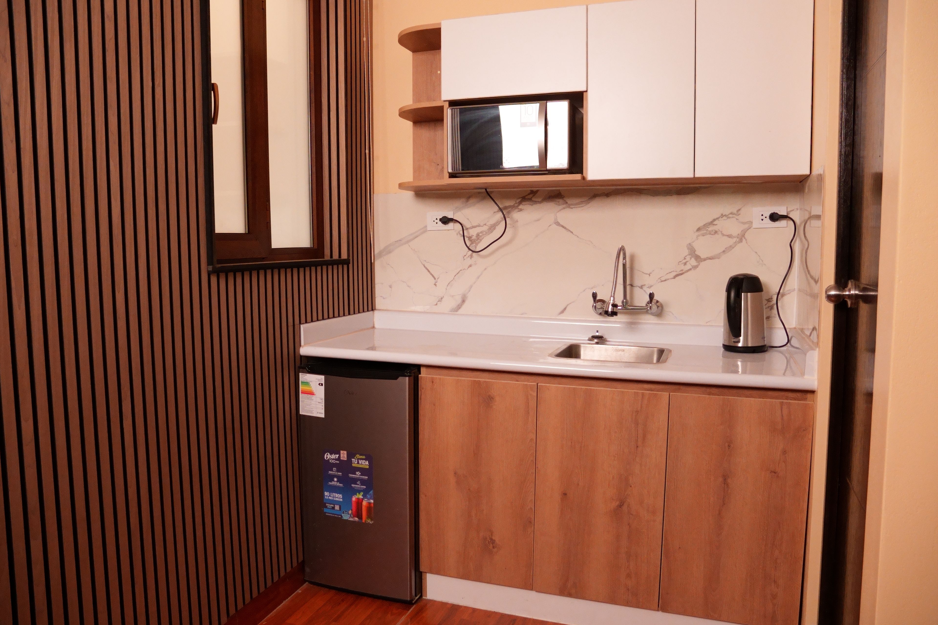 Una cocina compacta con refrigerador integrado, un lavamanos y un microondas.