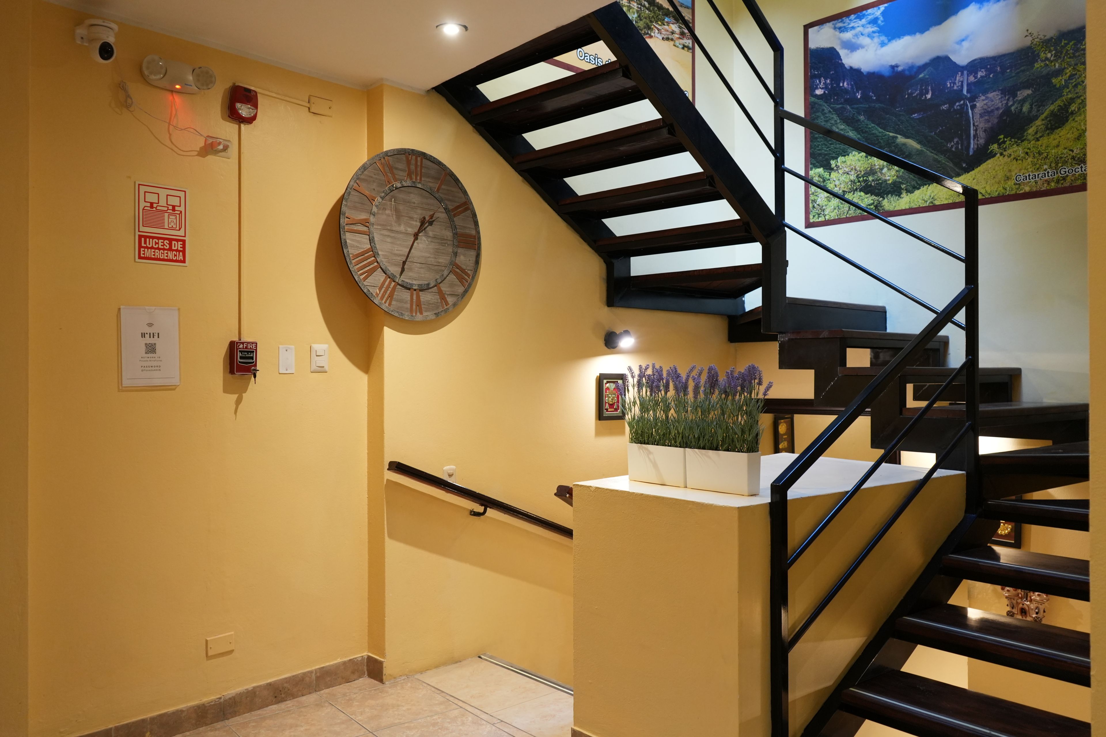 A staircase with a wooden handrail and a black metal railing, leading to a landing with a wall-mounted clock and a framed picture.