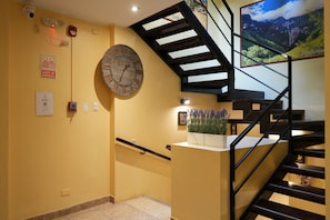 Una escalera con barandilla de madera y pasamanos de metal negro, que conduce a un rellano con un reloj de pared y un cuadro enmarcado.