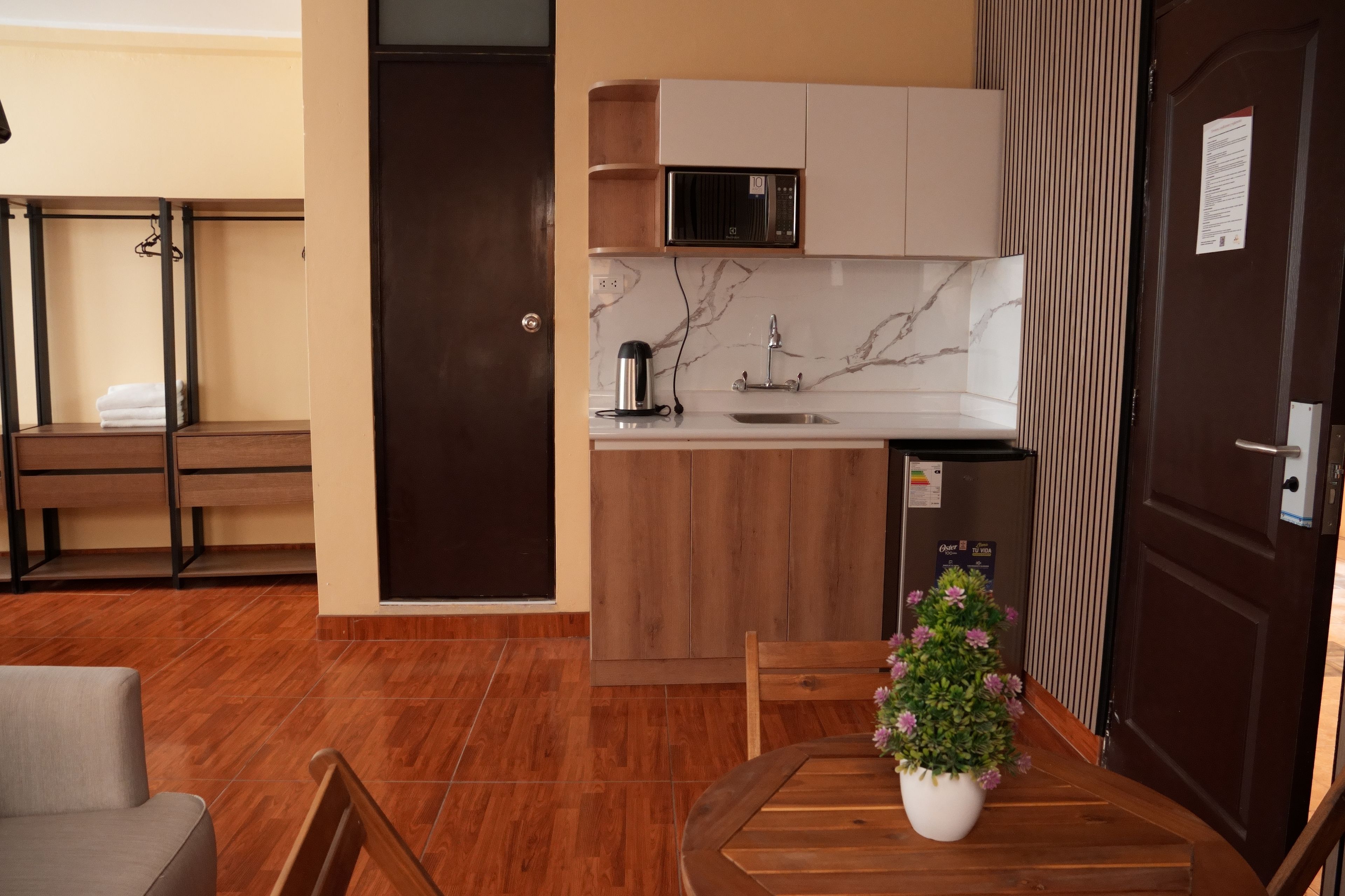 Cocina compacta con microondas integrado, un lavabo y una pequeña encimera. Hay una mesa de comedor de madera con una planta en maceta.