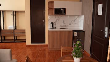 Cocina compacta con microondas integrado, un lavabo y una pequeña encimera. Hay una mesa de comedor de madera con una planta en maceta.