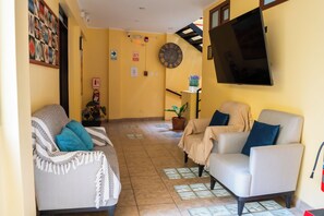 A living room with two sofas, a mounted TV, and a clock on the wall. - Posada Miraflores (Lima)