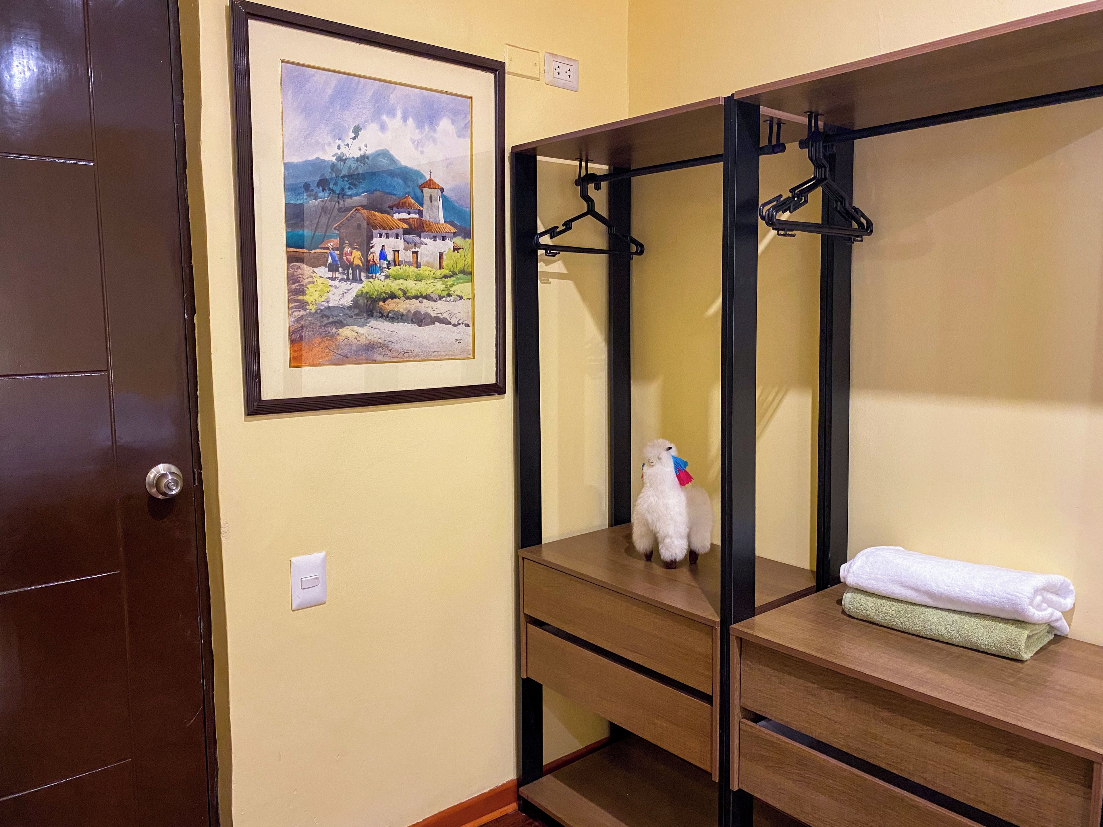 Quarto com cama, pintura emoldurada, toalha e um pequeno cão branco.