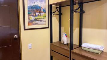 Quarto com cama, pintura emoldurada, toalha e um pequeno cão branco.