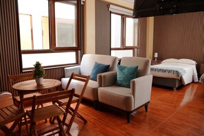 A hotel room with a bed, two armchairs, a wooden table, and a potted plant. - Posada Miraflores (Lima)