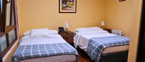A hotel room with two beds, a wooden floor, a painting on the wall, and a window with a view.