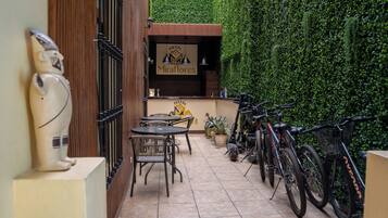 A patio area with a table and chairs, a bike rack with bicycles, and a wall with a green hedge.