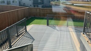 A deck with a wooden floor and metal railings, overlooking a grassy area and residential buildings. - Bonavista Light House Deluxe (Winnipeg)