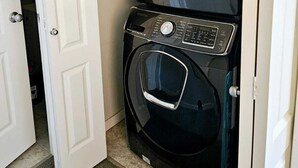 A compact washer and dryer unit in a small laundry room with a white door. - Bonavista Light House Deluxe (Winnipeg)