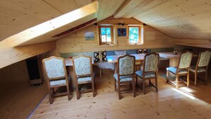 A cozy attic room with a wooden ceiling, a dining table with chairs, and a window with a view of the outdoors. - Relaxation on 2 levels; hiking,cycling from the house, skiing in the surrounding (Großweil)