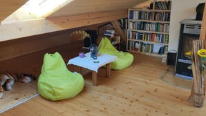 A cozy attic room with a wooden sloped ceiling, a bookshelf, a small table with a vase of sunflowers, and two bean bags. - Relaxation on 2 levels; hiking,cycling from the house, skiing in the surrounding (Großweil)