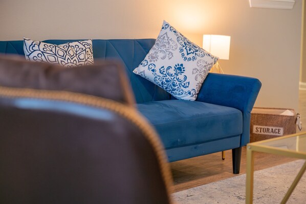 A blue sofa with patterned cushions, a glass coffee table, and a storage unit labeled "STORAGE" in a living room.