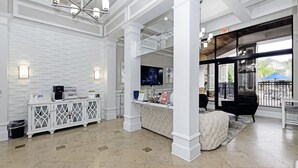 A spacious lobby with a white brick wall, a reception desk, a television, and a large window offering a view of the outdoors.
