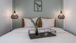 Une chambre à coucher comprenant un lit, deux lampes fixées au mur, un tableau encadré et une table de chevet avec un plateau et des verres.