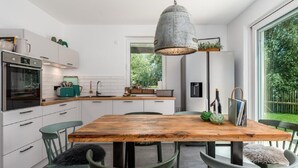 Une cuisine moderne avec des meubles blancs, une table à manger en bois et un luminaire suspendu de style industriel.