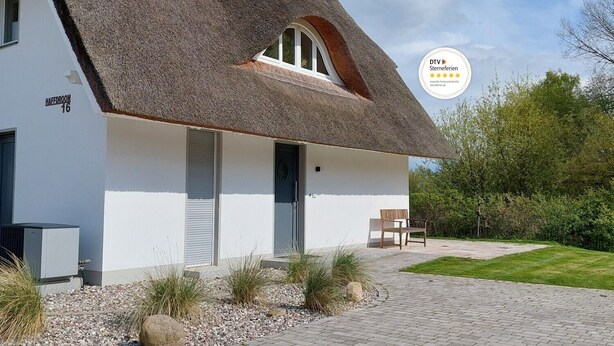 Une maison moderne avec un toit de chaume, un petit porche et un jardin.