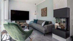 Un salon moderne avec un téléviseur à écran plat, un canapé, un fauteuil vert, une table basse et une cheminée.