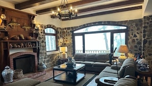A cozy living room with a stone fireplace, a large window, and a comfortable sofa. - Tudor Mountain Retreat (Panamá)