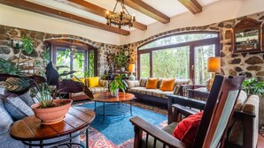A cozy living room with stone walls, wooden beams, large windows, and comfortable seating. - Tudor Mountain Retreat (Panamá)