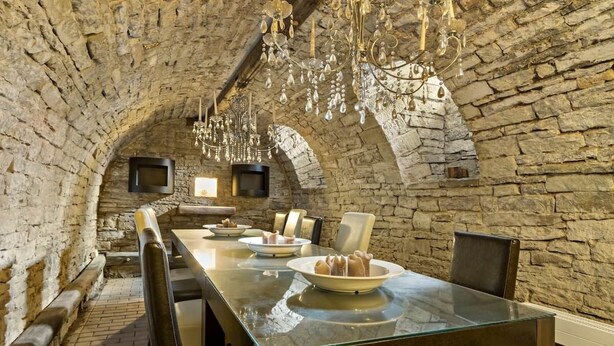 Un interior con una larga mesa, sillas, paredes de piedra y candelabros.
