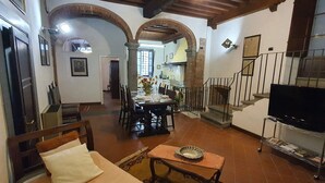 Amplia sala de estar con televisor, zona de comedor y cocina al fondo.