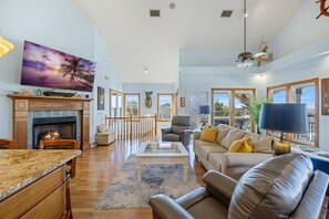 A spacious living room with a fireplace, a large window, and a ceiling fan.