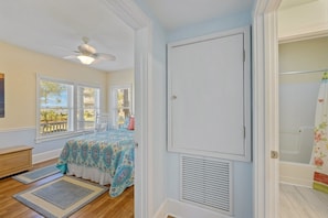 A bedroom with a bed, a ceiling fan, a window with blinds, a door, and a bathroom with a shower curtain. - Gulf View * Sunsets * Boat parking * King Bed * Walk to Downtown (Cedar Key)