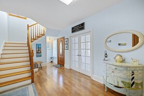 A hallway with a wooden staircase, a door with a sign, a mirror, and a decorative cabinet. - Gulf View * Sunsets * Boat parking * King Bed * Walk to Downtown (Cedar Key)