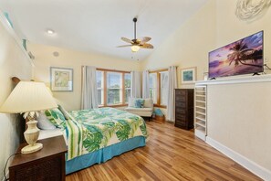 A bedroom with a bed, a ceiling fan, a TV, and a window with shutters.