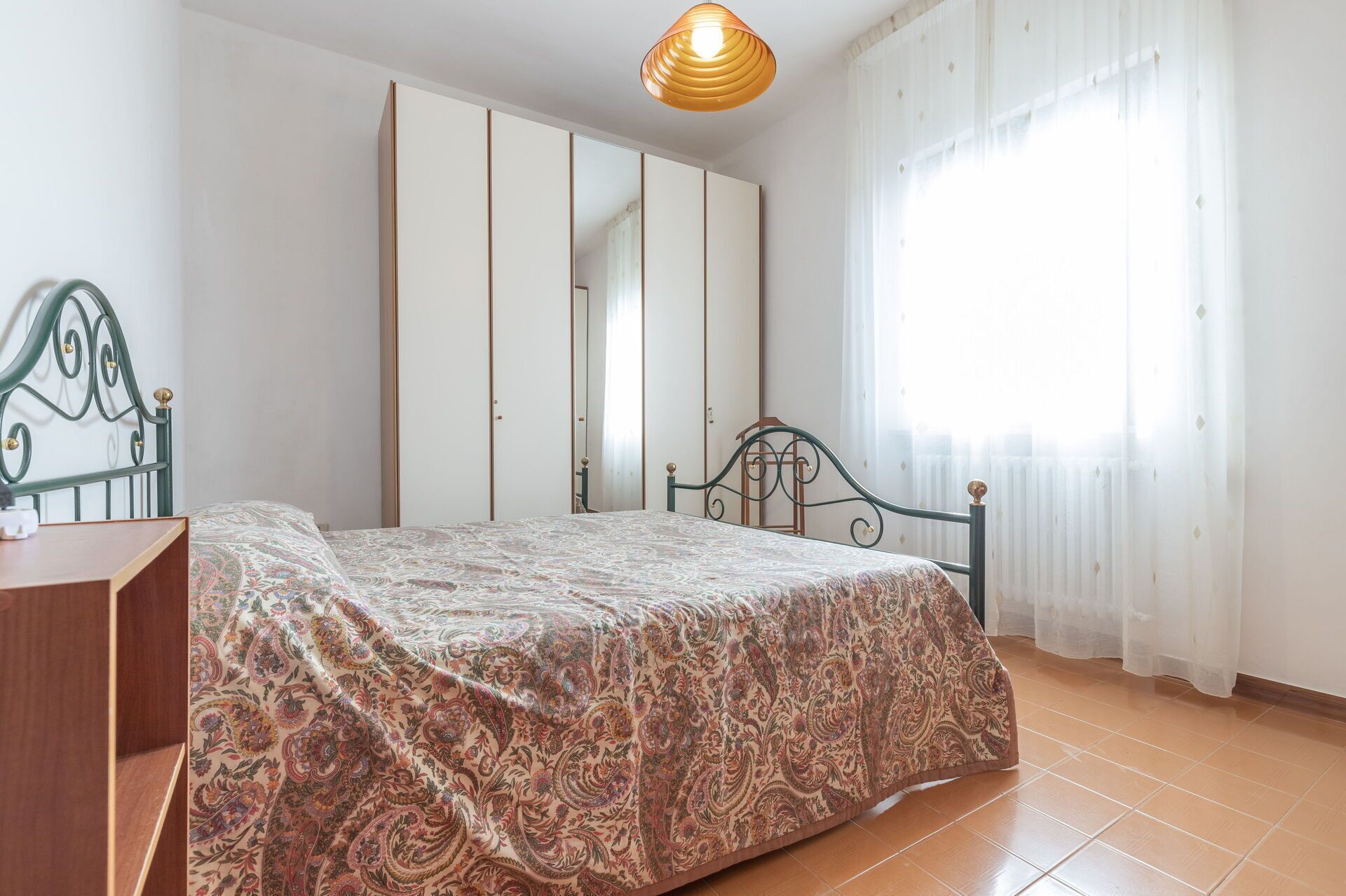 Une chambre à coucher avec un lit, une armoire, un bureau et une fenêtre avec des rideaux.