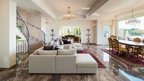 A spacious living room with a large grey sectional sofa, a dining area with ornate chairs, a chandelier, and a staircase with black railings. - Wonderful private villa for 10 people with private pool, A/C, WIFI, TV, terrace and panoramic view (Capo D'orlando)