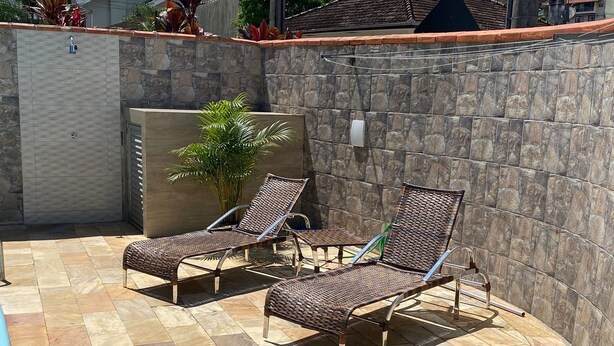 A poolside area with two wicker lounge chairs and a stone wall. - Blumen Espaço (Blumenau)