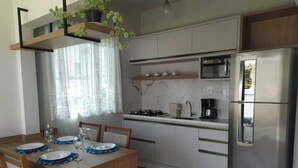 A modern kitchen with white cabinets, a stainless steel refrigerator, and a dining table set with plates and glasses. - Blumen Espaço (Blumenau)