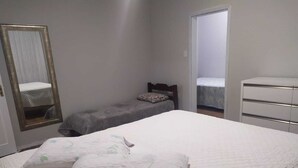 A bedroom with a large bed, a bedside table, a dresser, and a mirror. - Blumen Espaço (Blumenau)