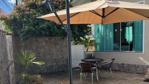 A backyard with a swimming pool, a patio table with chairs, a potted plant, and a large umbrella. - Blumen Espaço (Blumenau)