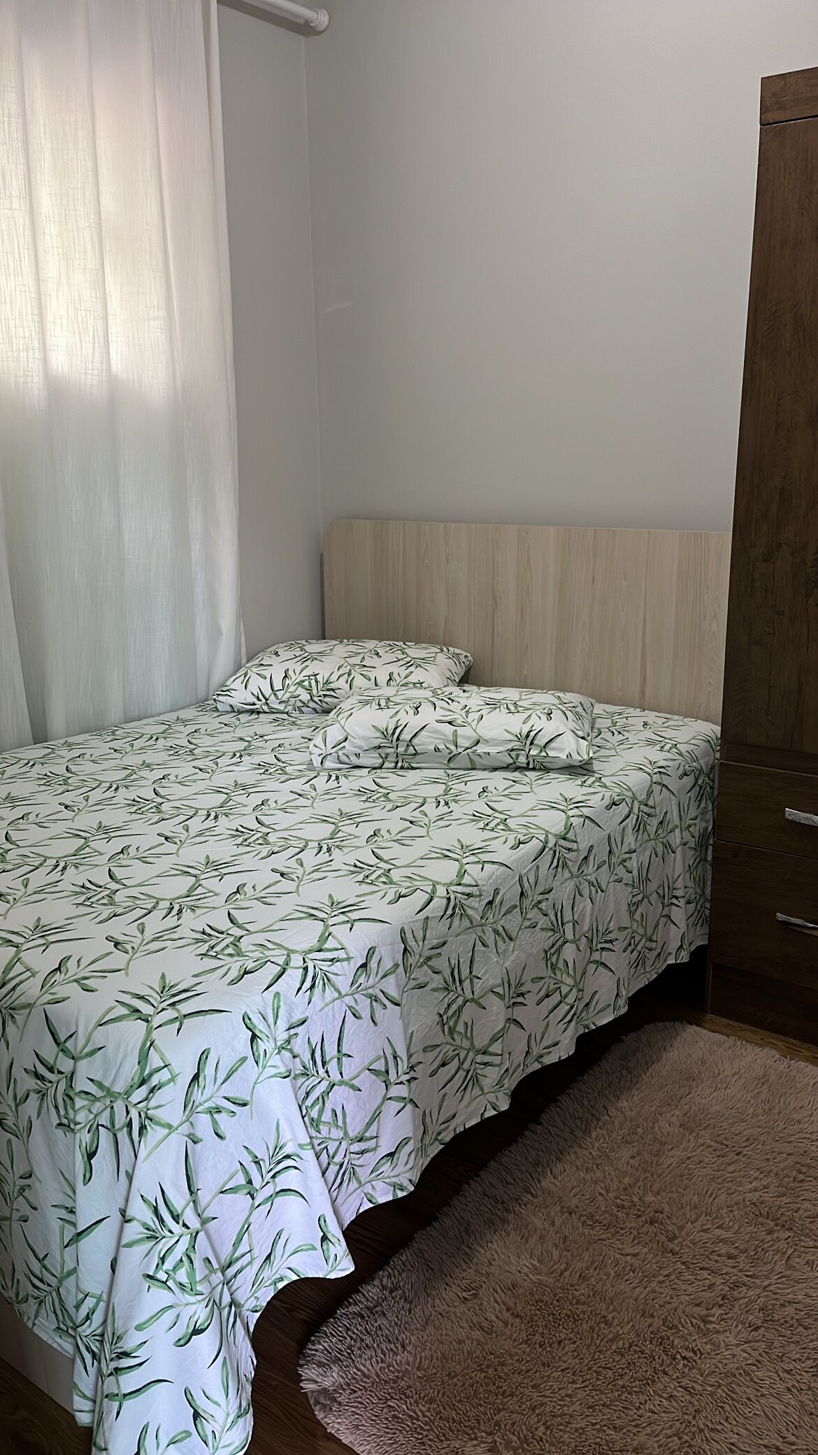 Quarto com cama, guarda-roupa de madeira e tapete fofinho.