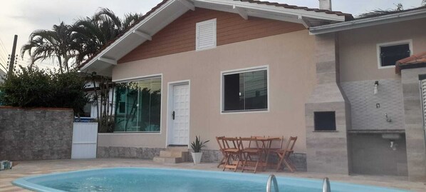 A house with a swimming pool, a patio with wooden furniture, and a stone wall.