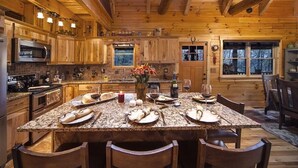 A rustic wooden cabin kitchen with a large island, wooden cabinets, and a stone countertop.