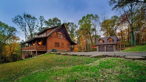 A large log cabin with a balcony, a smaller attached garage, and a well-maintained lawn.