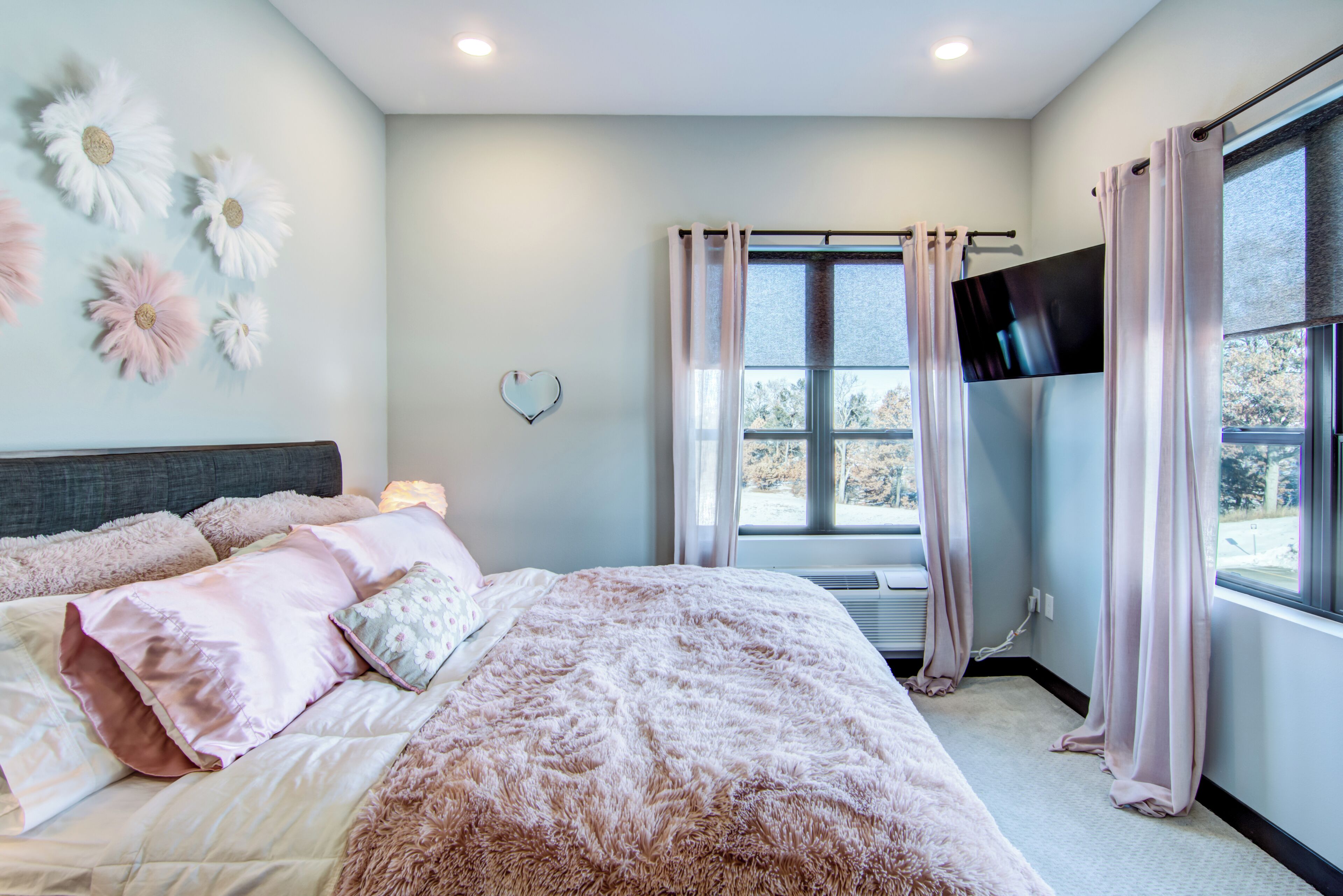 Une chambre à coucher avec un grand lit, un téléviseur à écran plat fixé au mur et une fenêtre avec des rideaux.