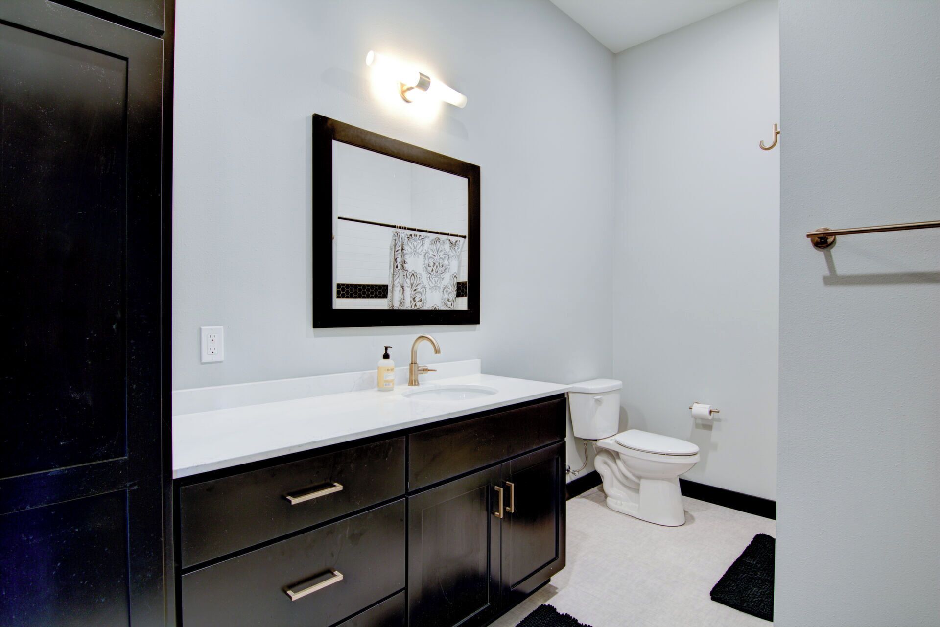 A modern bathroom with a white sink, dark cabinetry, a large mirror, and a toilet.