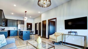 Un espacio de estar moderno con cocina, sofá, mesa de centro y televisor.