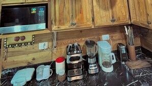Cozinha com armários de madeira, micro-ondas, torradeira, liquidificador e panelas penduradas.