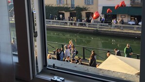 Une vue depuis une fenêtre donnant sur un canal, avec des bâtiments et des personnes.