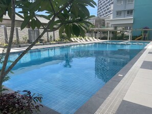 A swimming pool with tiled edges, surrounded by lounge chairs and a stone wall. - Mesavirre Bacolod | Elegantly Furnished 1BDM w/ Balcony @ LOPEZ LUX. (Bacolod)