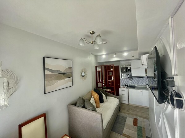A modern living room with a sofa, a dining area with a kitchen in the background, and a ceiling light fixture. - Mesavirre Bacolod | Elegantly Furnished 1BDM w/ Balcony @ LOPEZ LUX. (Bacolod)