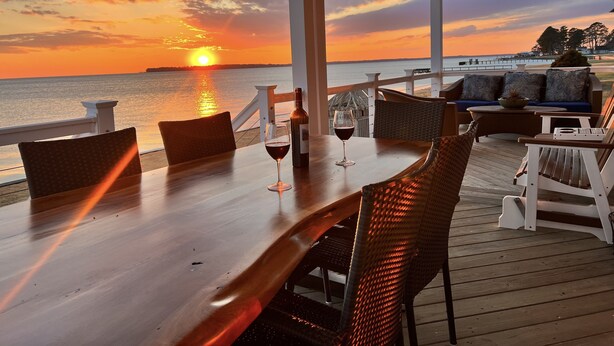 Una terraza de madera con una mesa y sillas, con vista al atardecer sobre el agua.