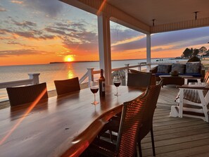 Une terrasse en bois avec une table et des chaises, d’où l’on peut admirer le coucher de soleil sur l’eau.