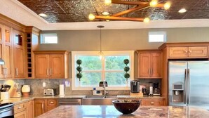 Una cocina moderna con armarios de madera, una isla grande con taburetes de bar, un refrigerador de acero inoxidable y un diseño de techo único.